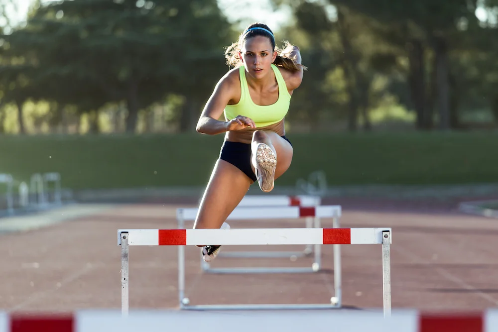 An athlete jumps over a hurdle on a track