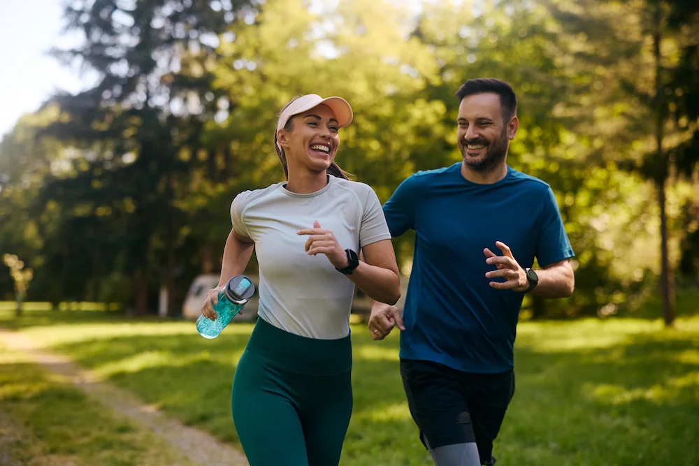A man and a woman smile while running side by side on a running trail